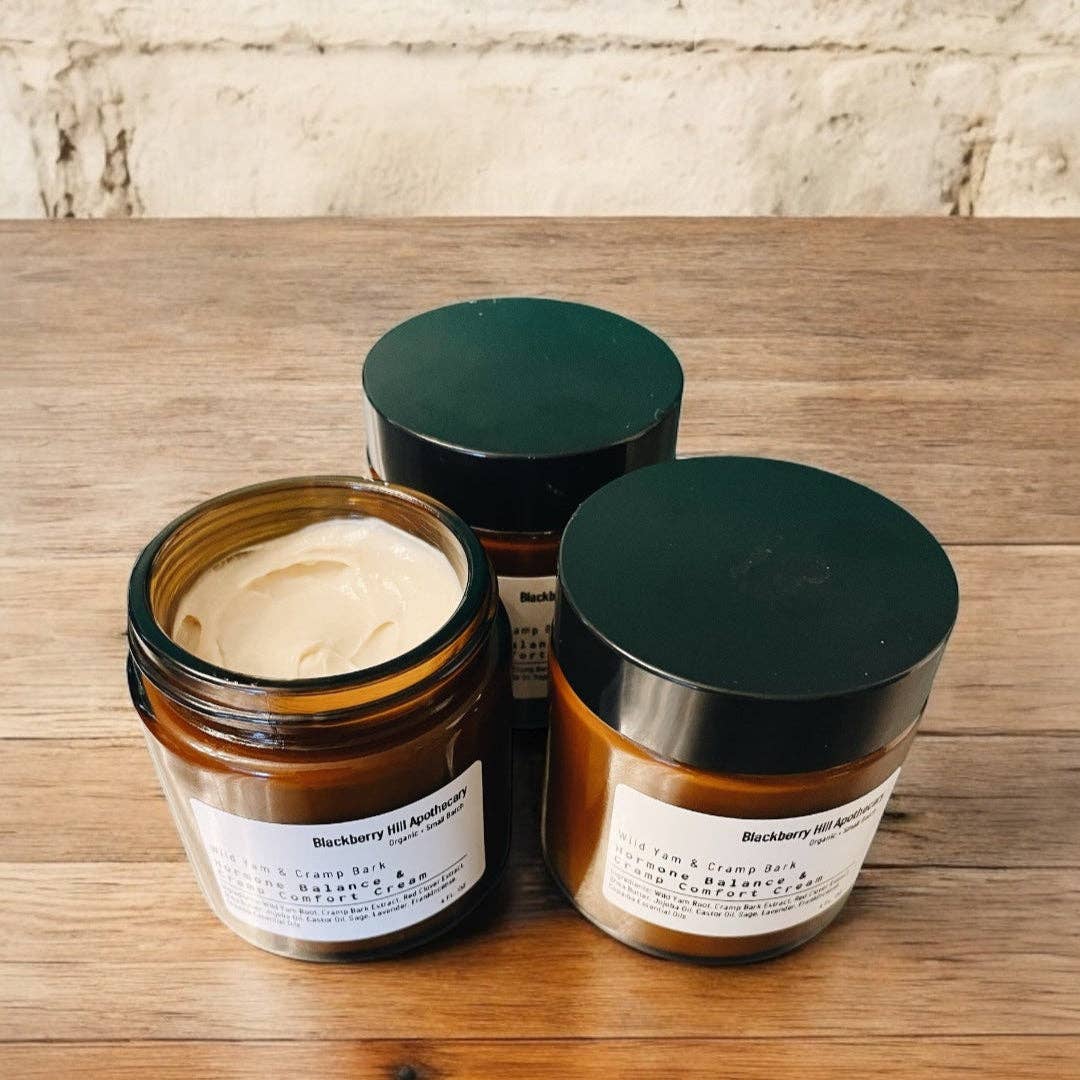 Three jars of cream or paste with green lids on a wooden surface.