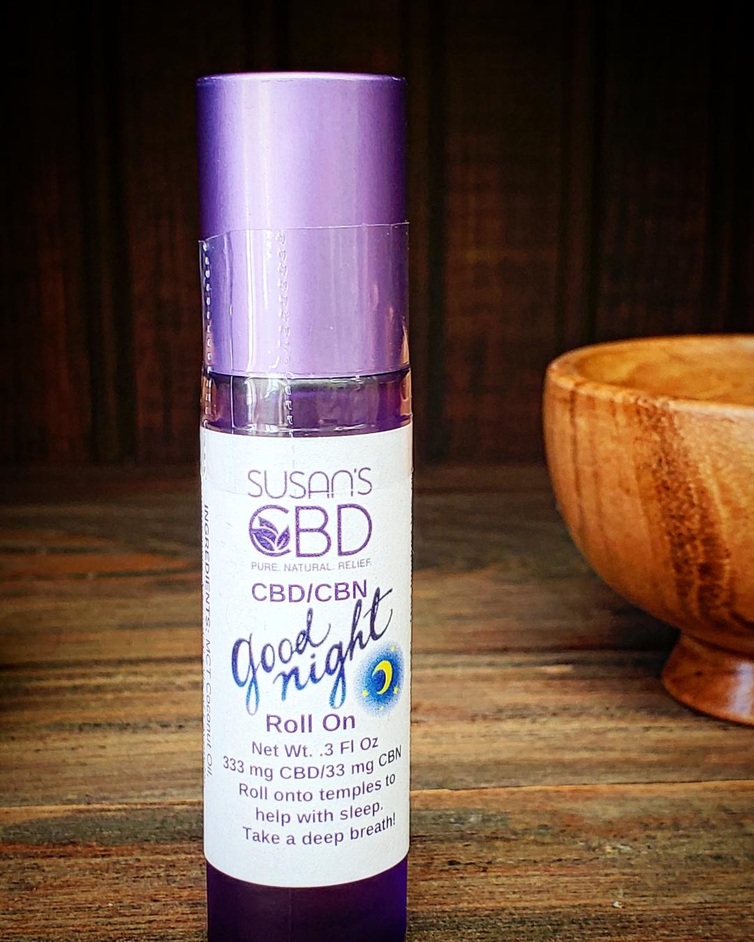 A roll-on bottle of Susan's Good Night sleep aid, with a purple cap and label displaying the product information. The bottle is placed in front of a wooden background.