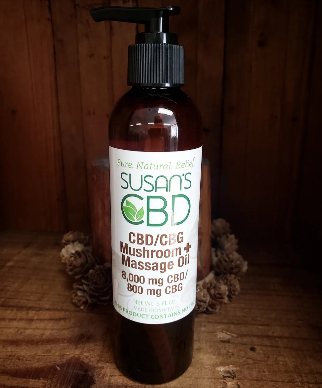 A bottle of Susan's CBD/CBG/Mushroom Massage Oil on a wooden surface with a pump dispenser. The label indicates the product contains 1000 mg of CBD and 100 mg of CBG.