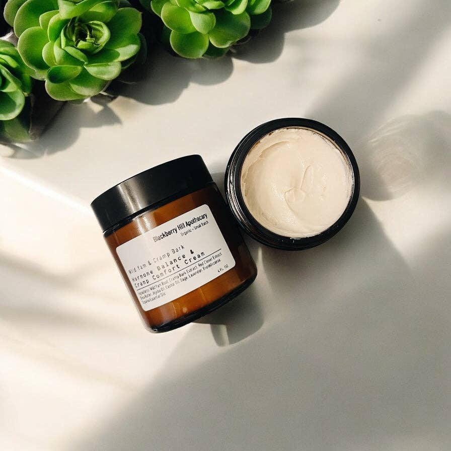 Two skincare products on a light surface with green plants in the background